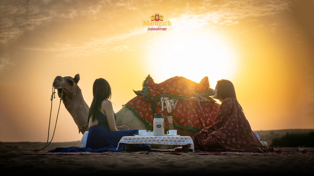 Women enjoying desert tea beside camel during sunset